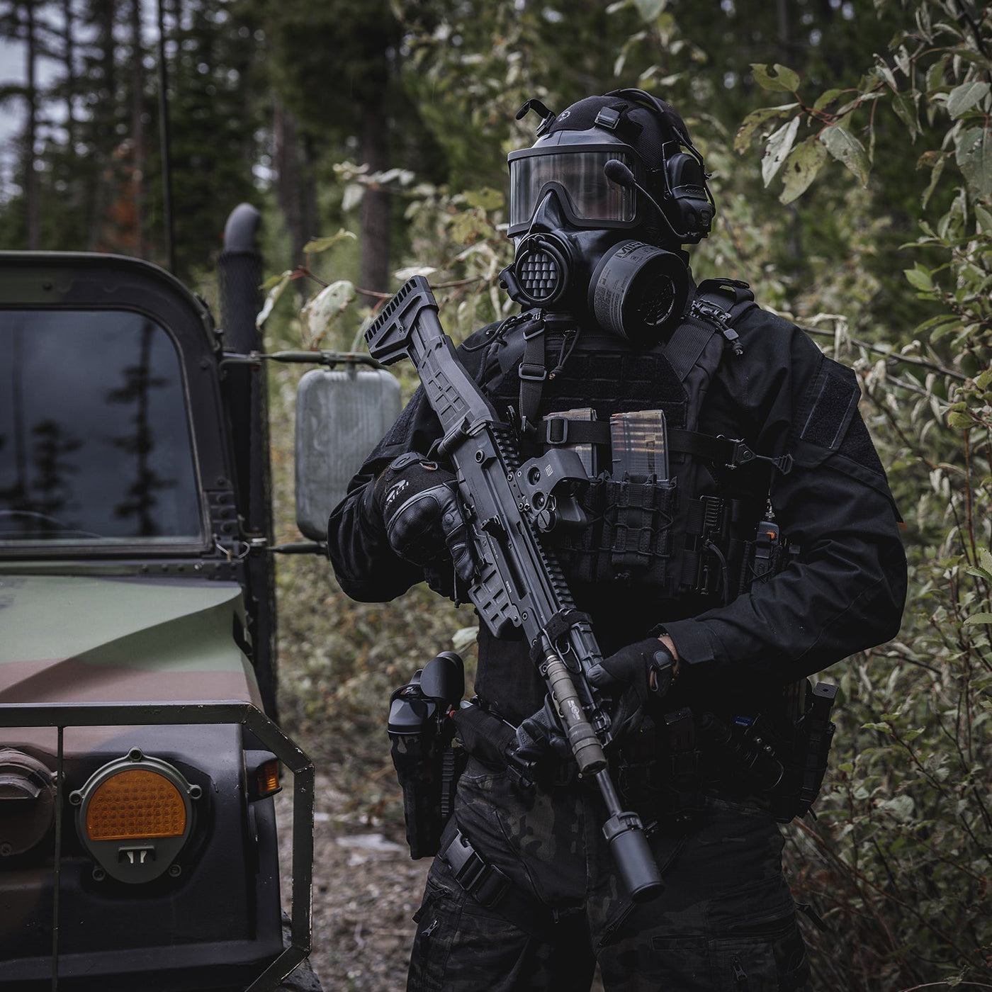 3/4 shot of a man in full tactical equipment wearing a CM-8M gas mask, holding an assault rifle.