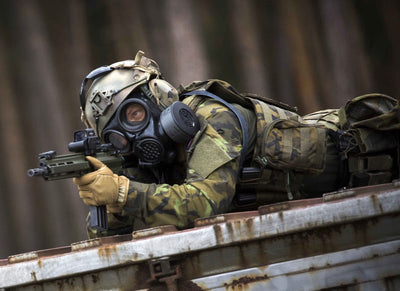Soldier laying down while aiming through a rifle, while wearing the CM-7M military mask